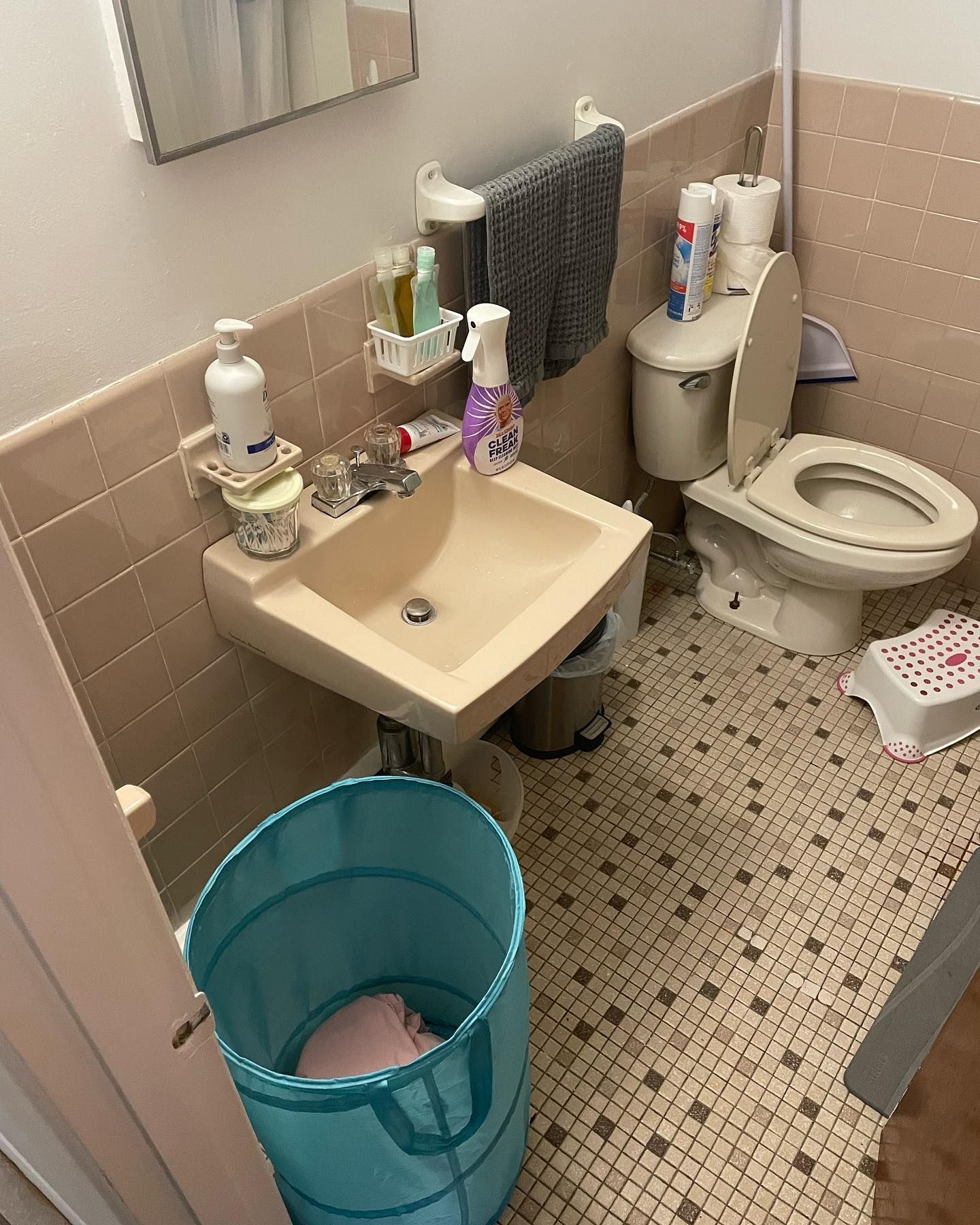 Small bathroom with toilet, sink, and laundry hamper. Beige and white tile floors and walls.