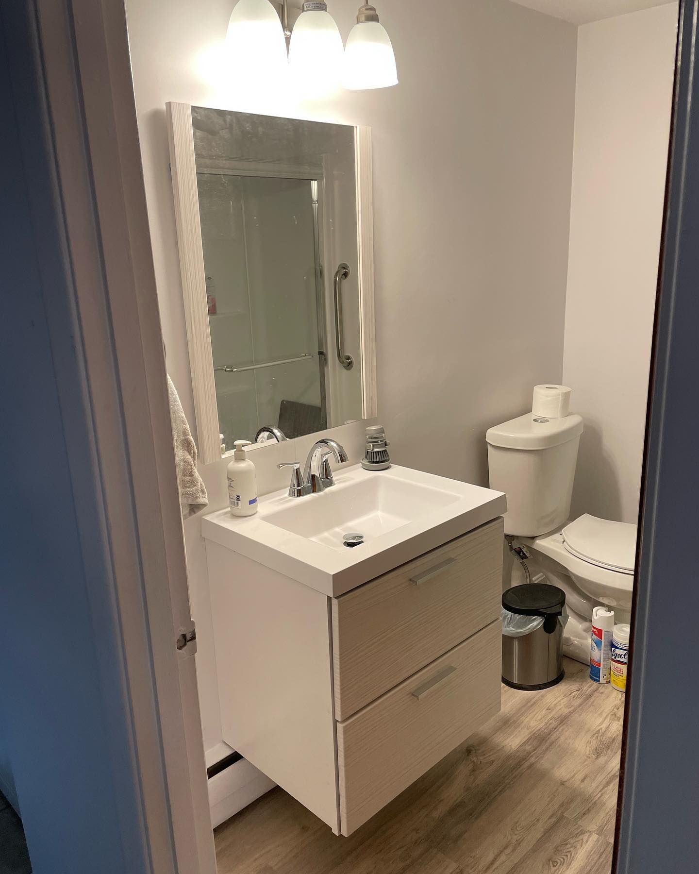 Small bathroom with a white vanity, toilet, and mirror. White walls and light-colored flooring.