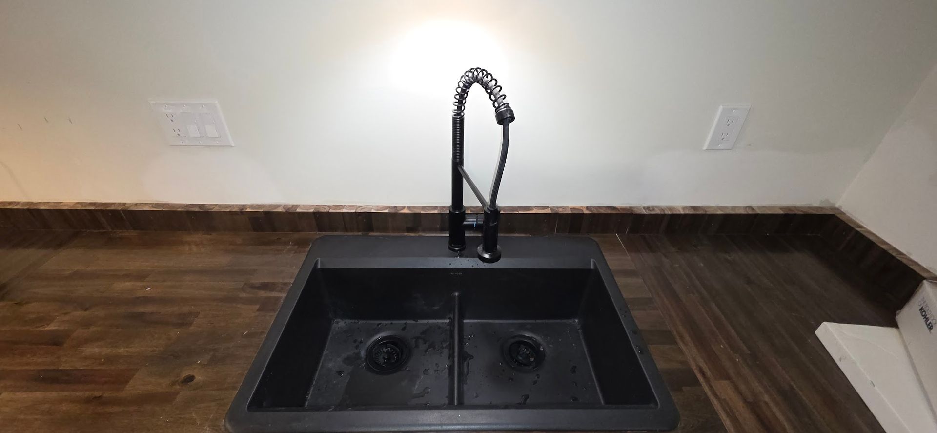 Black double basin sink with black faucet on a wooden countertop. Cream-colored walls.
