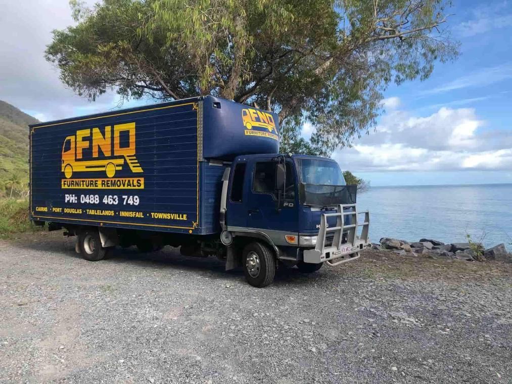 A Blue Moving Truck is Parked on the Side of the Road Next to a Tree — FNQ Furniture Removals in Cairns, QLD