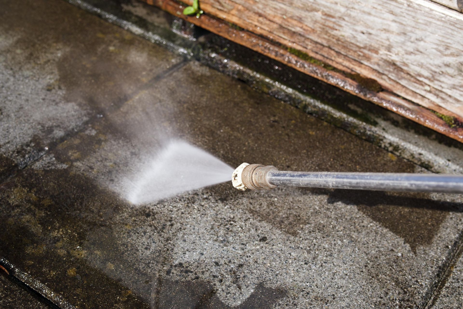 A person is using a high pressure washer to clean a sidewalk.