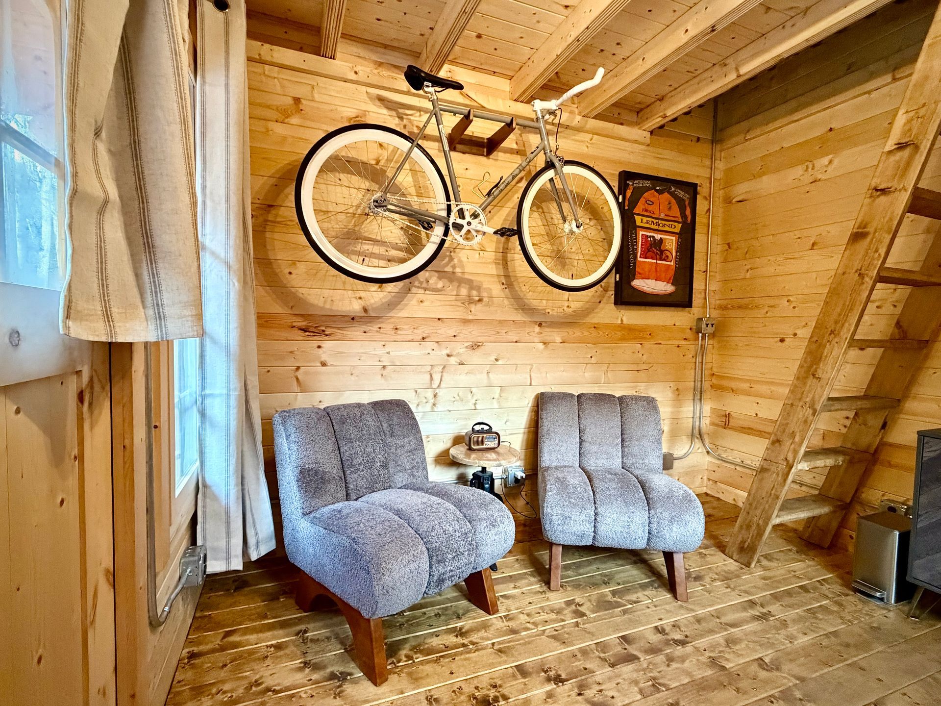 Cozy wooden room with two gray chairs, a bicycle on the wall, and a framed artwork.