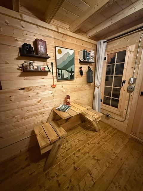 Cozy wooden sauna room with benches, wall shelves, and a framed mountain print beside a glass door.