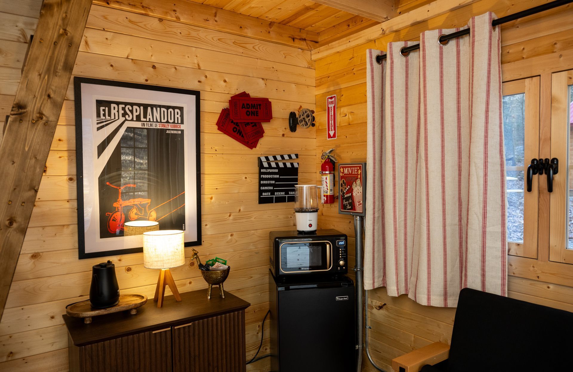 Cozy wood-paneled room with lamp-lit dresser, mini fridge, curtains, wall art, and TV.