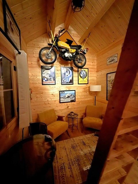 Motorcycle mounted on a wood-paneled wall above a cozy cabin-style seating area with framed art and a lamp