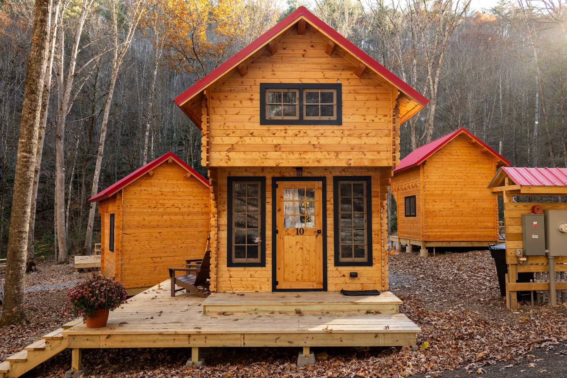 Rustic orange cabin with red trim and a front porch in a wooded autumn setting