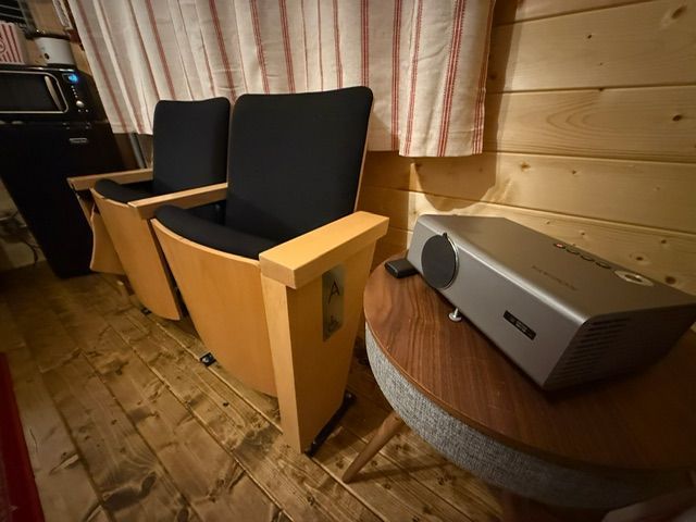 Two black chairs in a wood-paneled cabin beside a table with a projector and a laptop on the left.