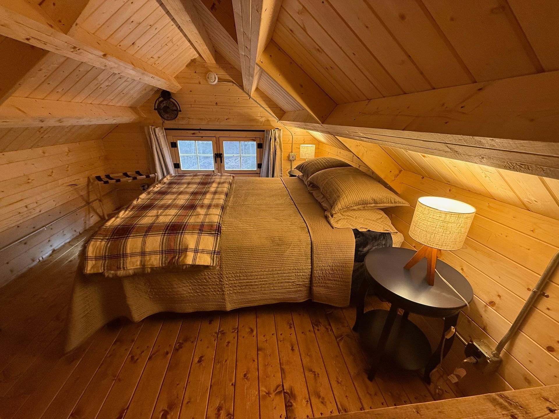 Cozy attic bedroom with a bed, wood-paneled walls, small window, and bedside lamp.