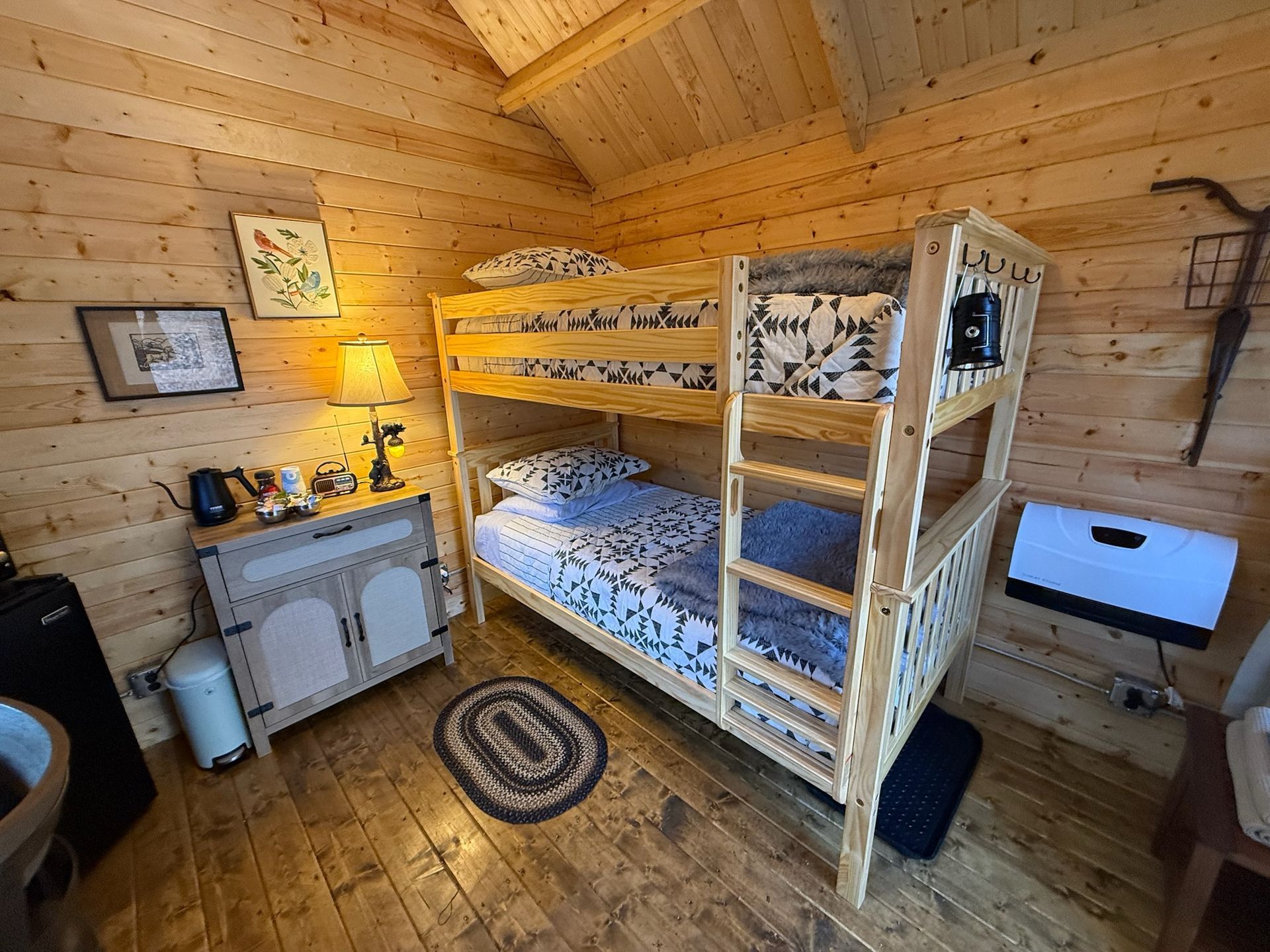 Wooden cabin bedroom with bunk bed, lamp-lit dresser, and rustic decor