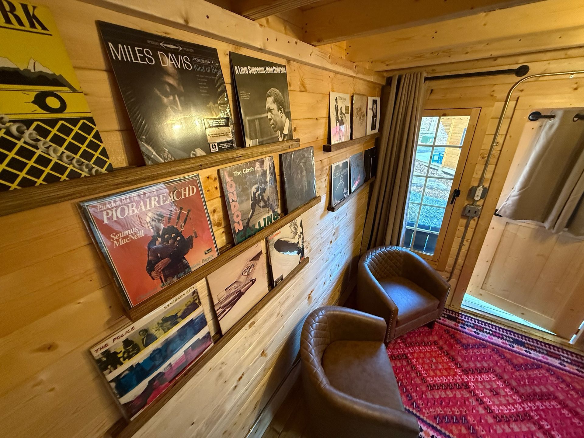 Record-lined room with two brown chairs, red rug, and a glass door to a snowy outside scene