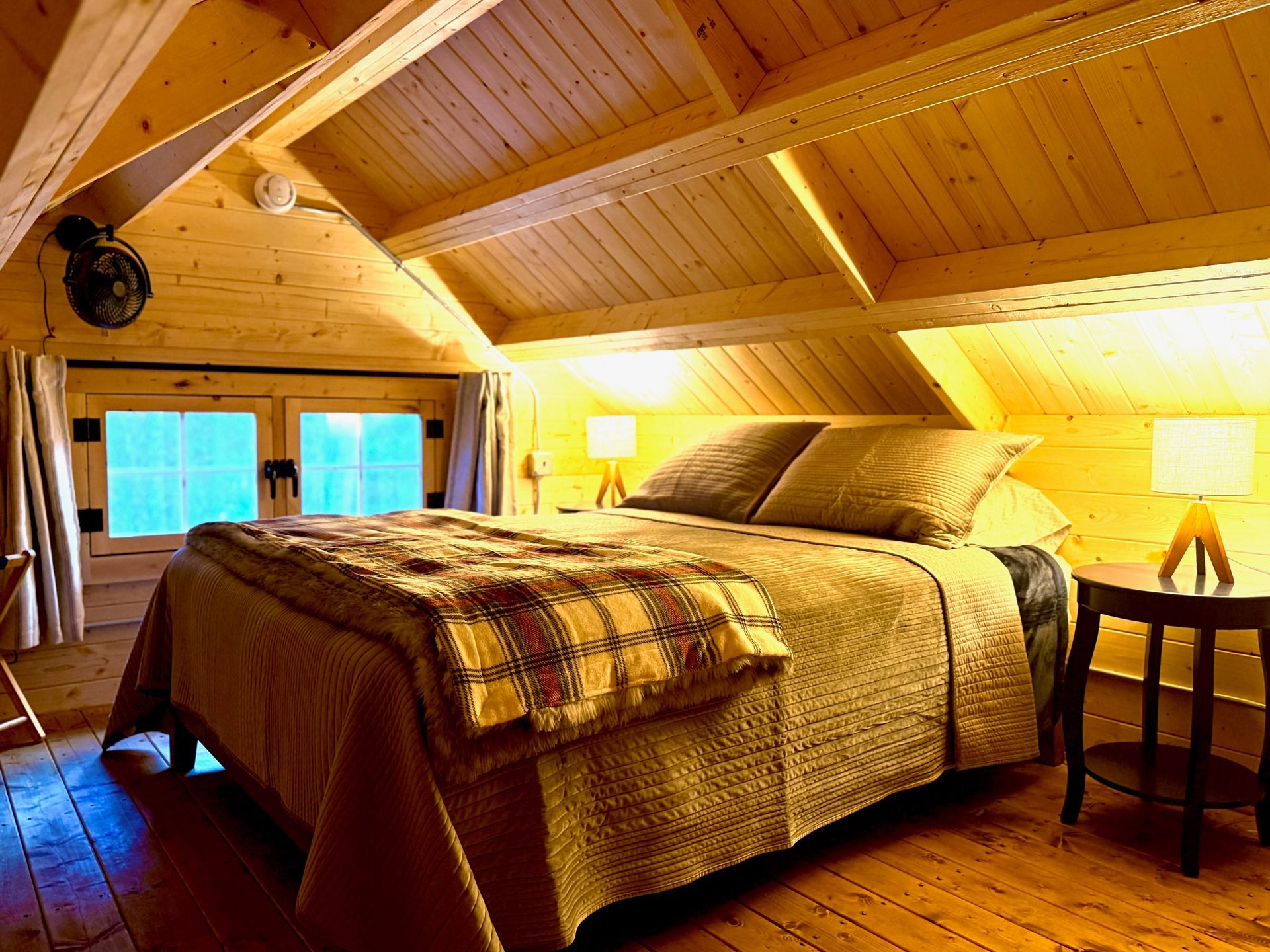 Cozy wooden bedroom with vaulted ceiling, king bed, warm lamp light, and bedside table.