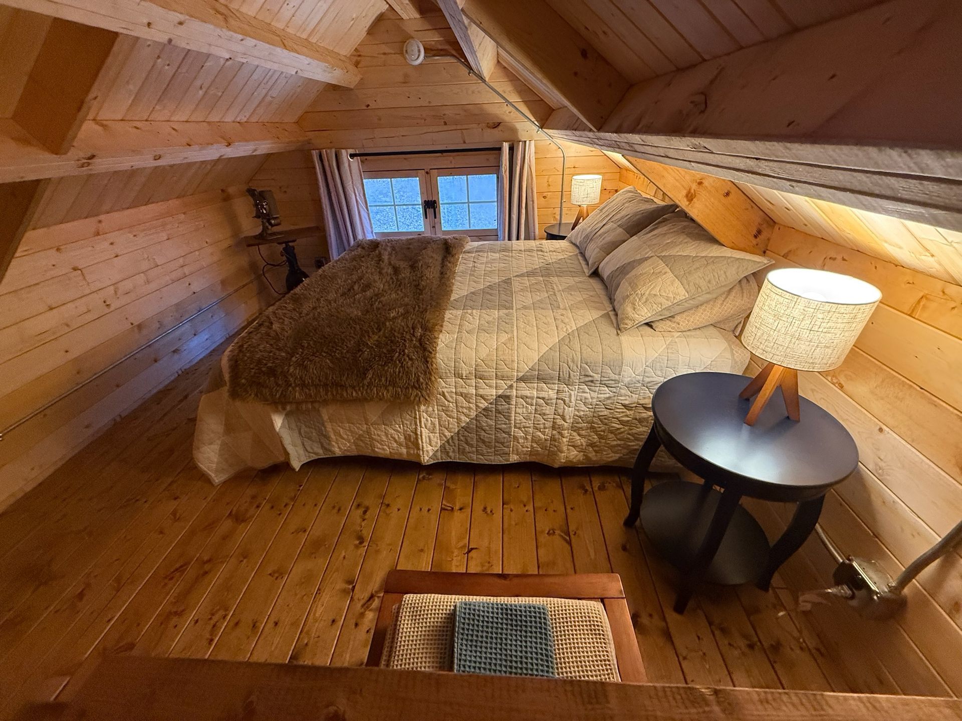 Cozy attic bedroom with a bed, bedside lamp, and wooden paneled walls and ceiling.