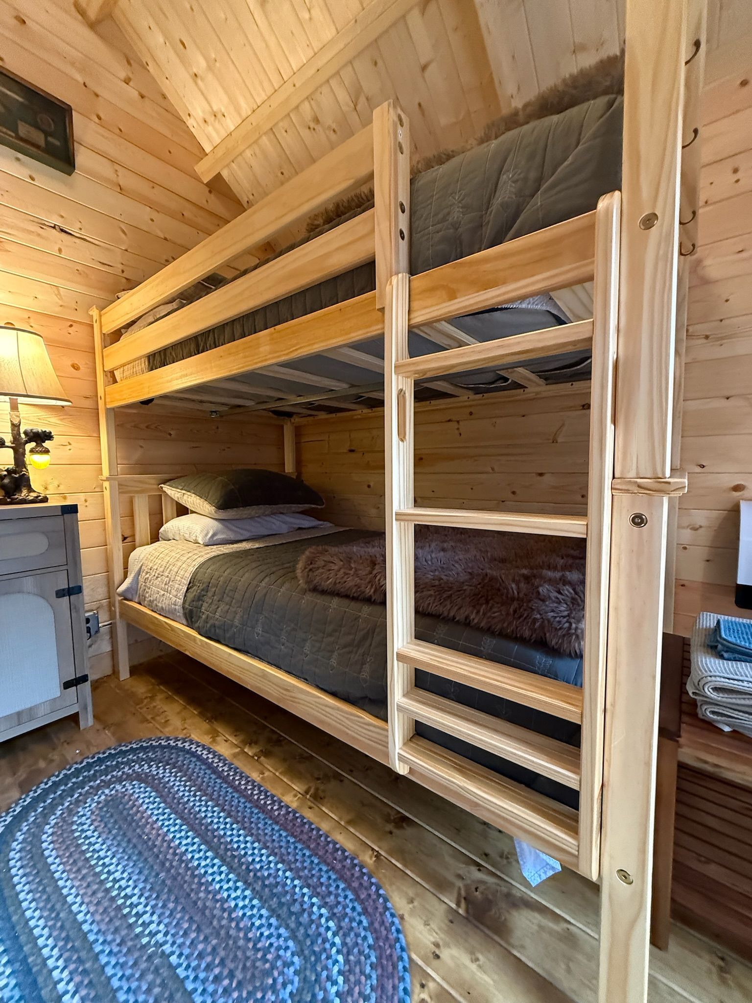 Wooden bunk bed in a cozy log cabin bedroom with striped bedding and a blue oval rug on the floor