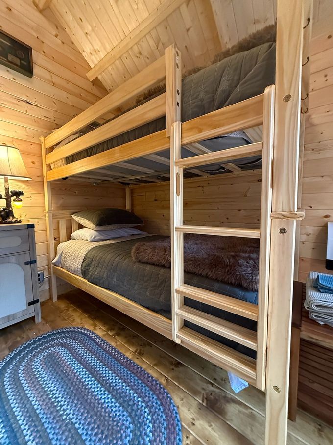 Wooden bunk beds in a cozy cabin bedroom with gray bedding and a blue braided rug.