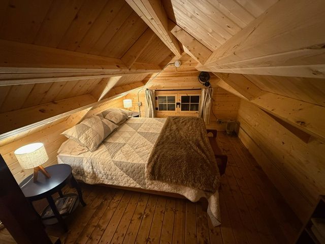 Cozy wooden attic bedroom with a bed, bedside table, and sloped cedar ceiling