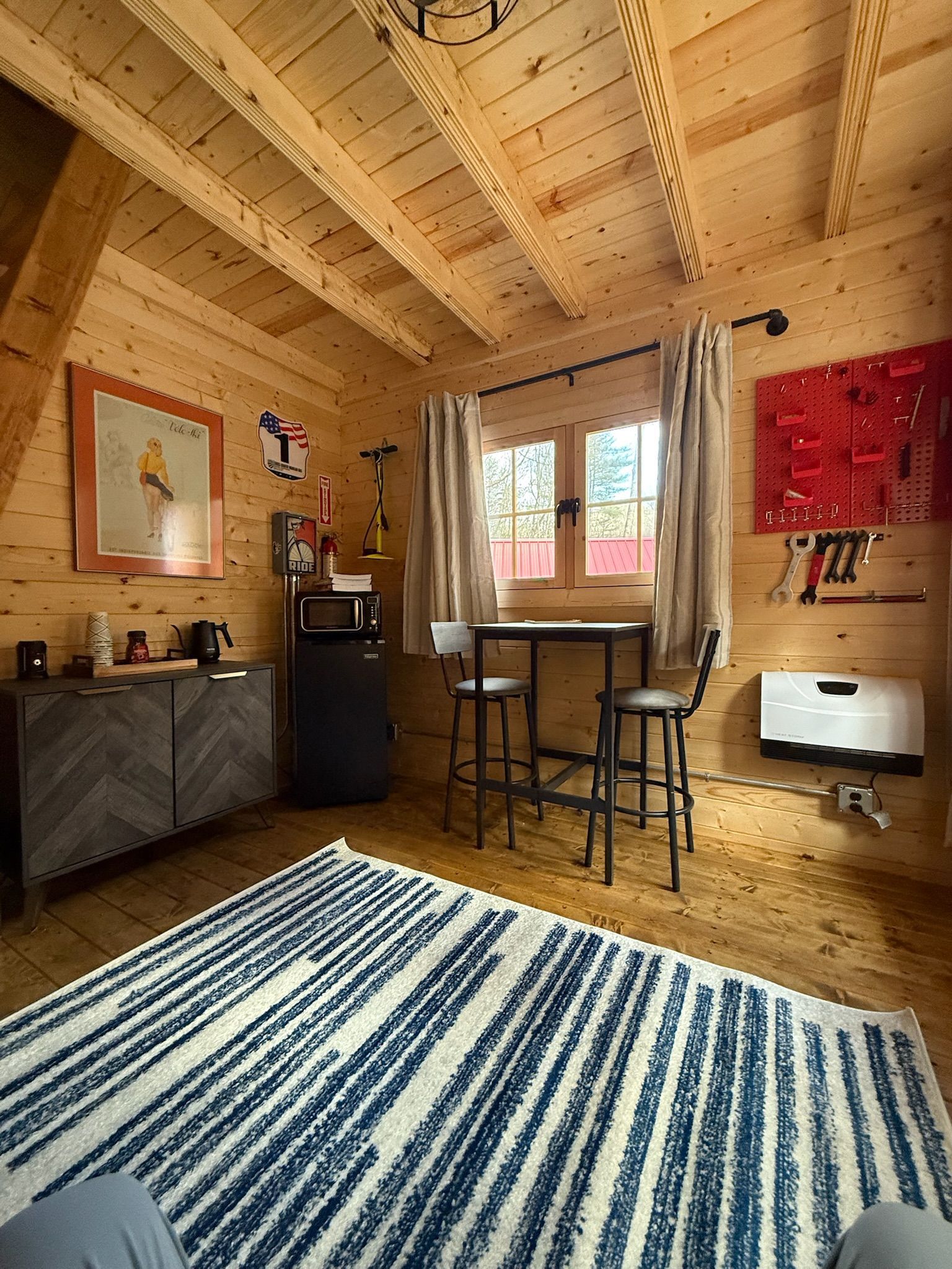 Cozy wooden cabin interior with desk, chair, rug, window, and red wall art