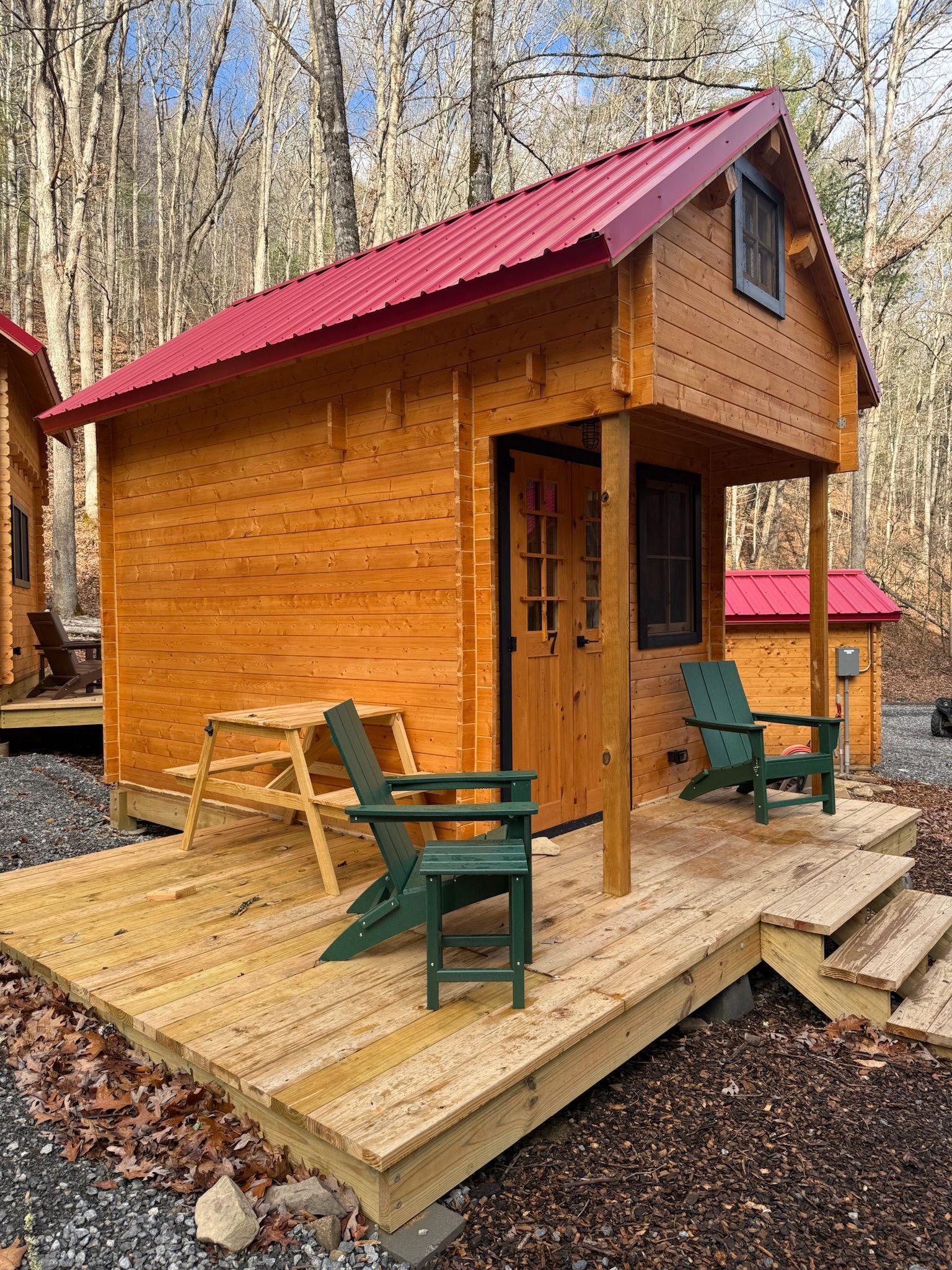 Small wooden cabin with red roof and porch chairs in a wooded setting