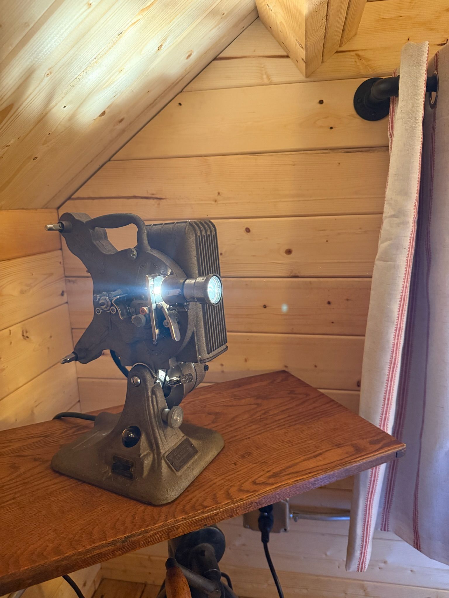 Crumpled metallic sculpture on a wicker table in a small wood-paneled attic room.