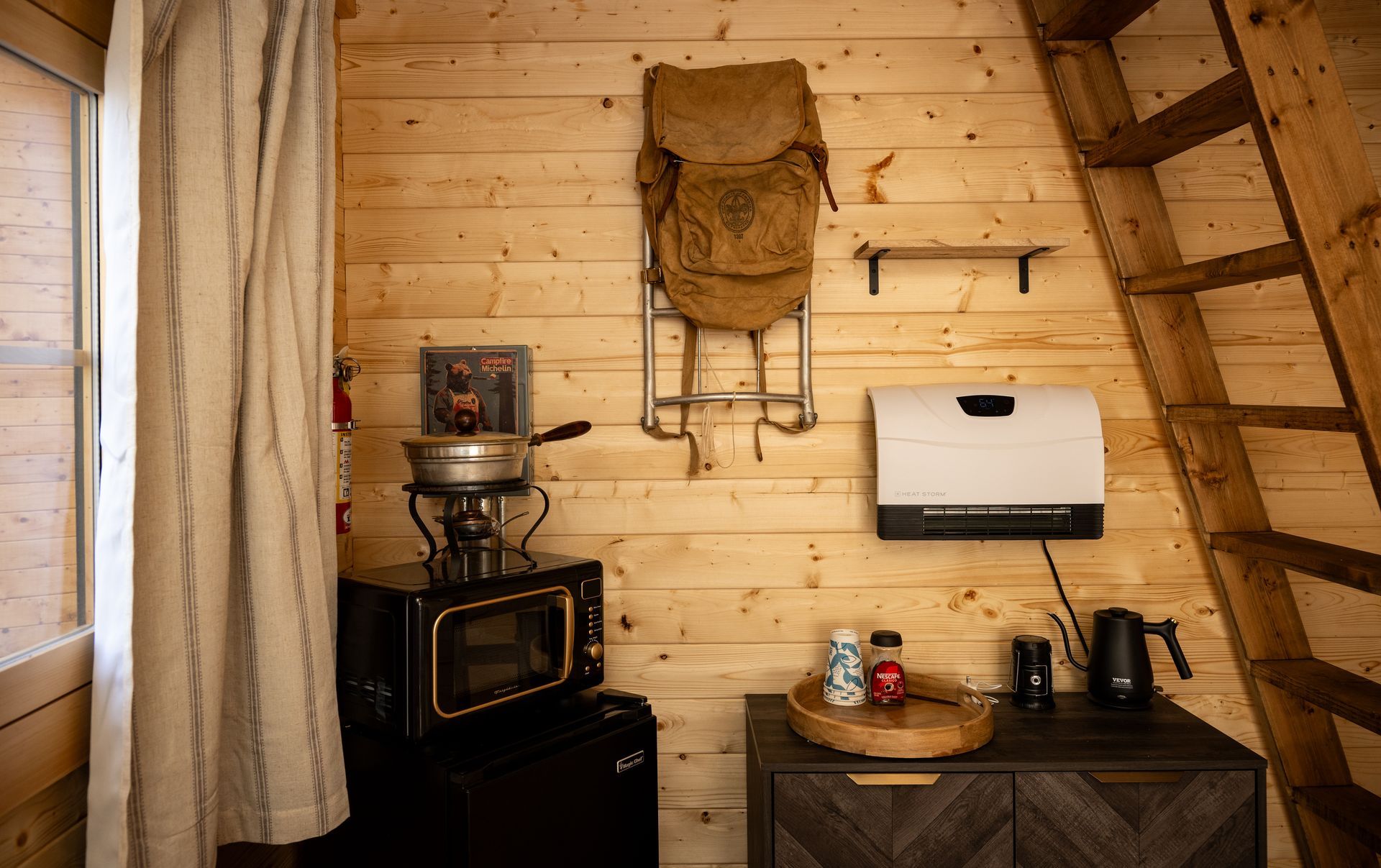 Cozy wooden cabin corner with stove, backpack on wall, paper towel holder, and ladder overhead.