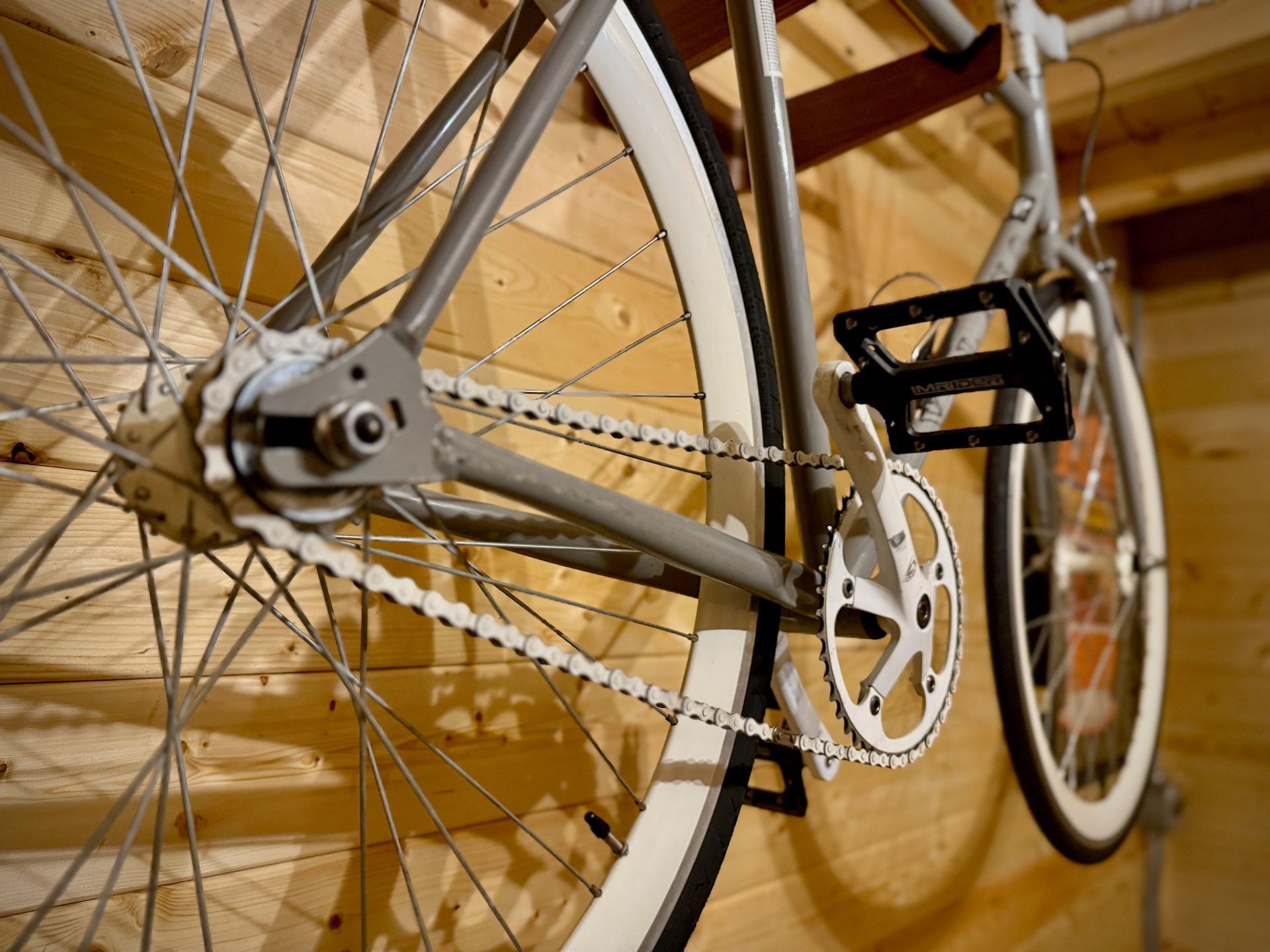 Close-up of a silver bicycle’s rear wheel, chain, and pedals in a wooden garage