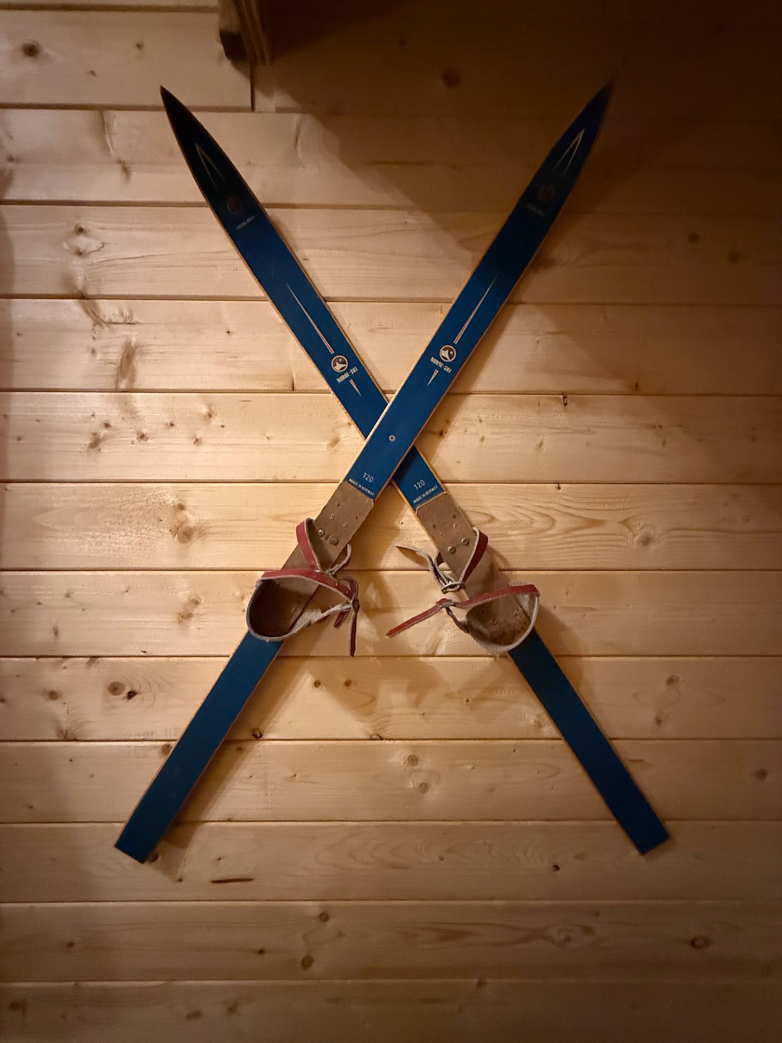 Two crossed blue skis with brown bindings mounted on a wooden wall