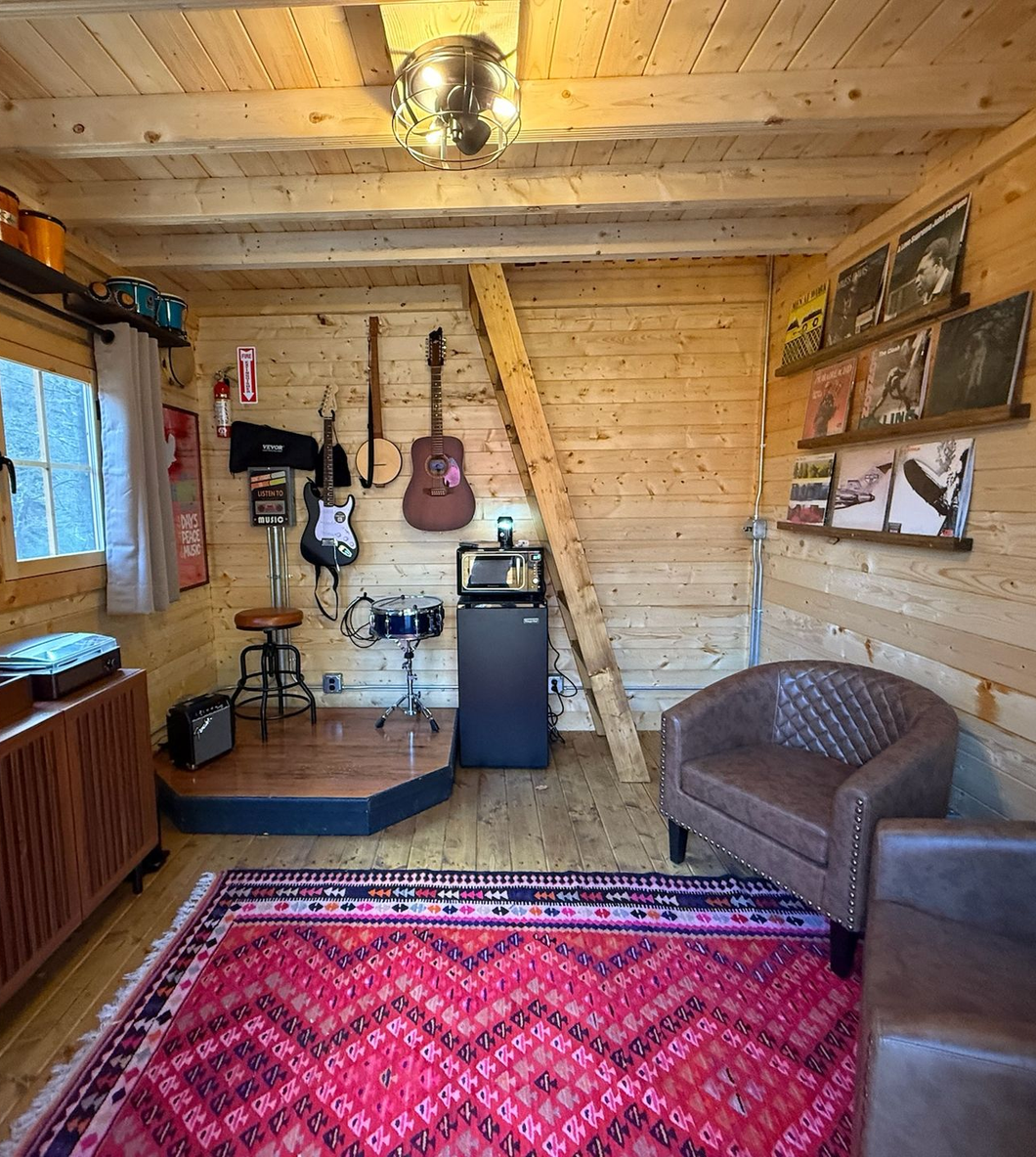 Cozy wooden cabin interior with red rug, guitar wall decor, chair, and window light