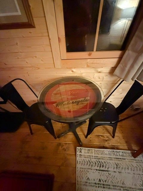 Small round table with two black chairs in a wooden room, near a window and a printed menu on the floor.