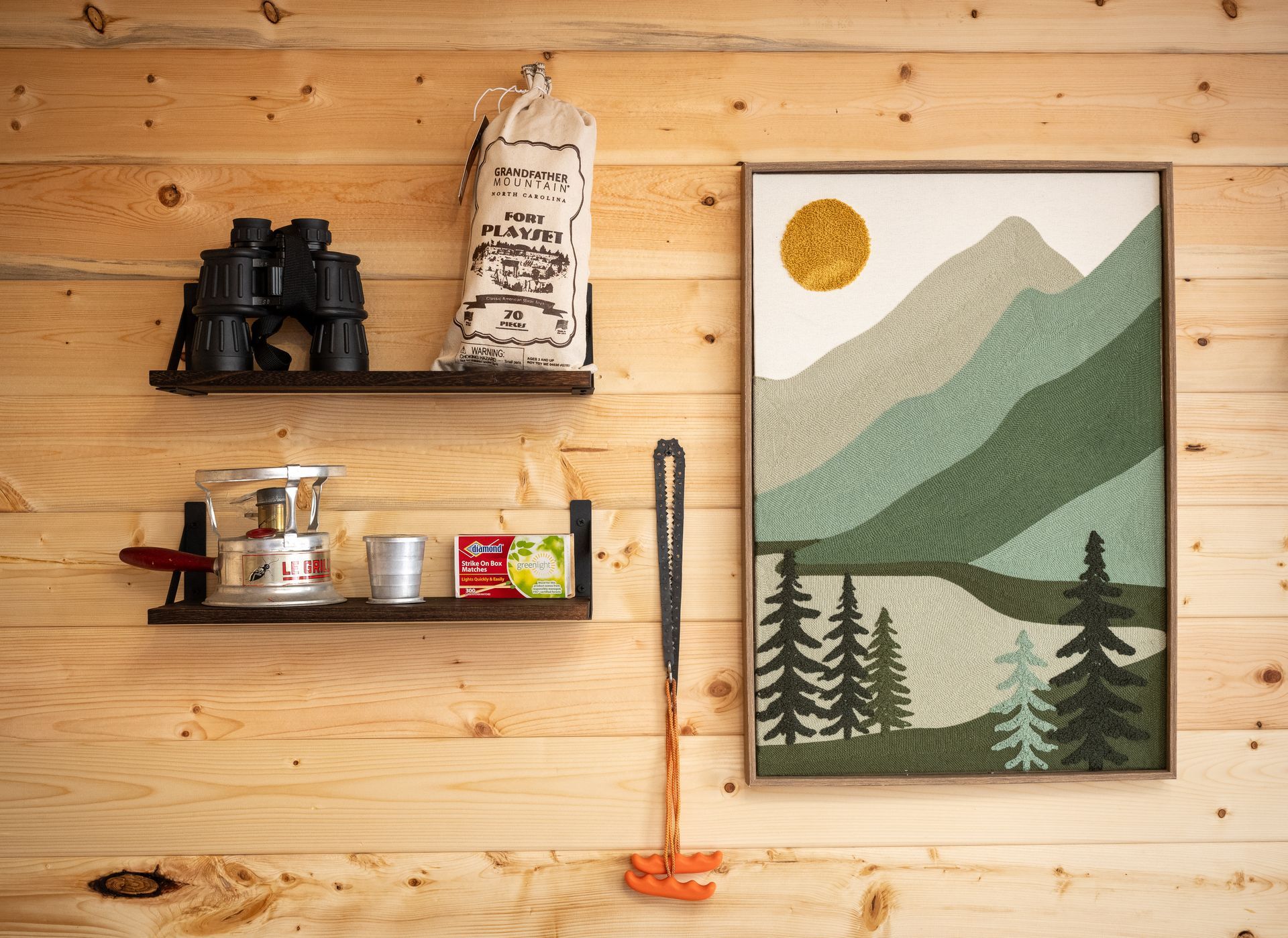 Wooden wall with shelves, jars, binoculars, a hanging broom, and a framed mountain landscape print.