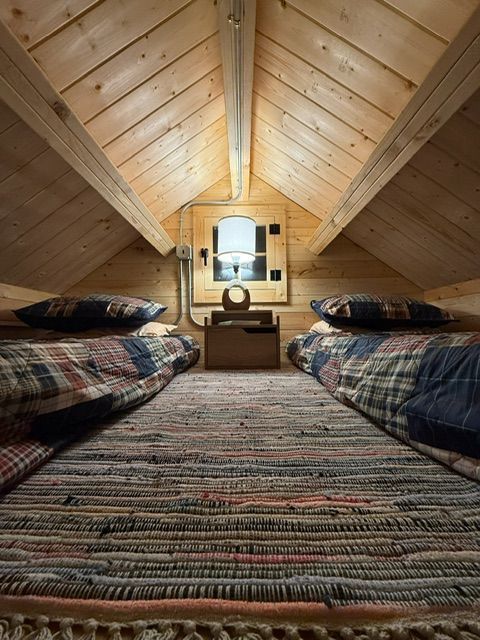 Cozy attic bedroom with twin beds, wooden paneled walls, and a small window at the far end