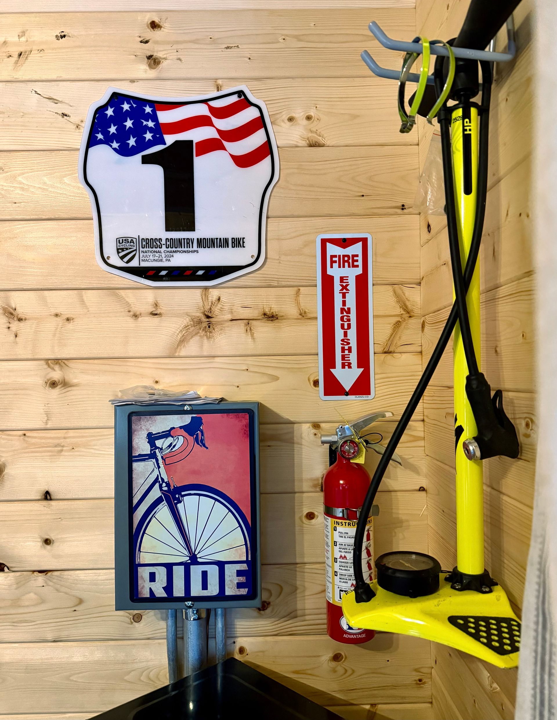 Wall with race memorabilia: American flag number 1 sign, RIDE sign, fire extinguisher, and yellow bike rack