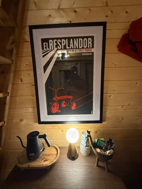 Warm wooden wall with framed poster, lit lamp, kettle, tray, and small basket on a shelf