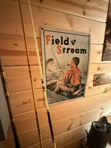 Framed “Field Stream” poster on a wooden cabin wall beside a coat rack