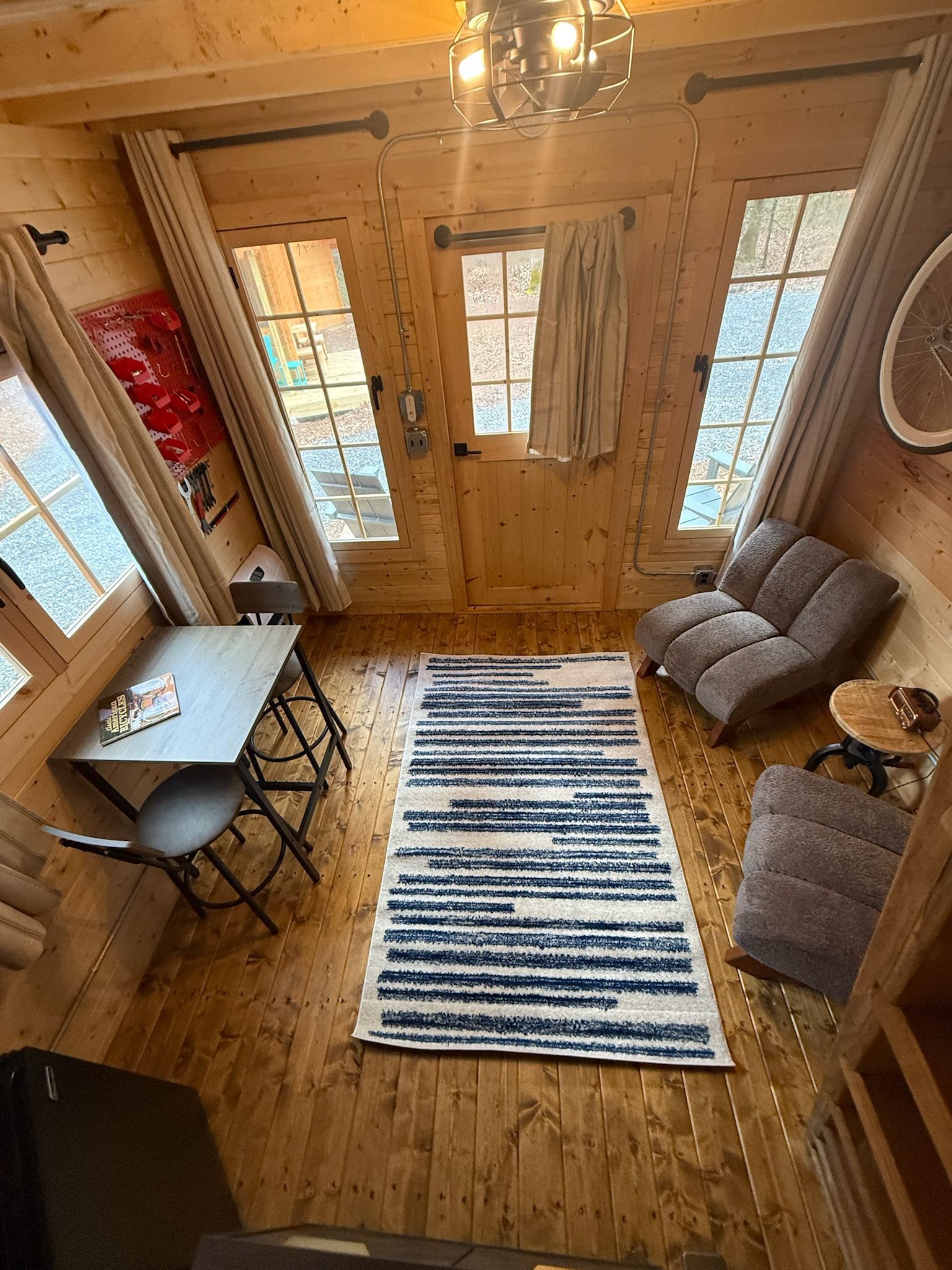 Cozy cabin interior with striped rug, small table, and cushioned chairs by wood-framed windows