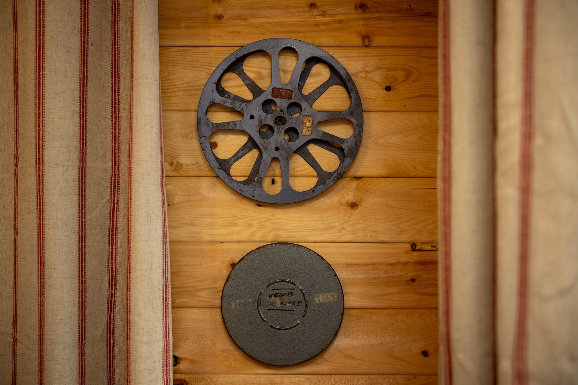 Two dark metal discs mounted on a wooden wall between beige curtains.