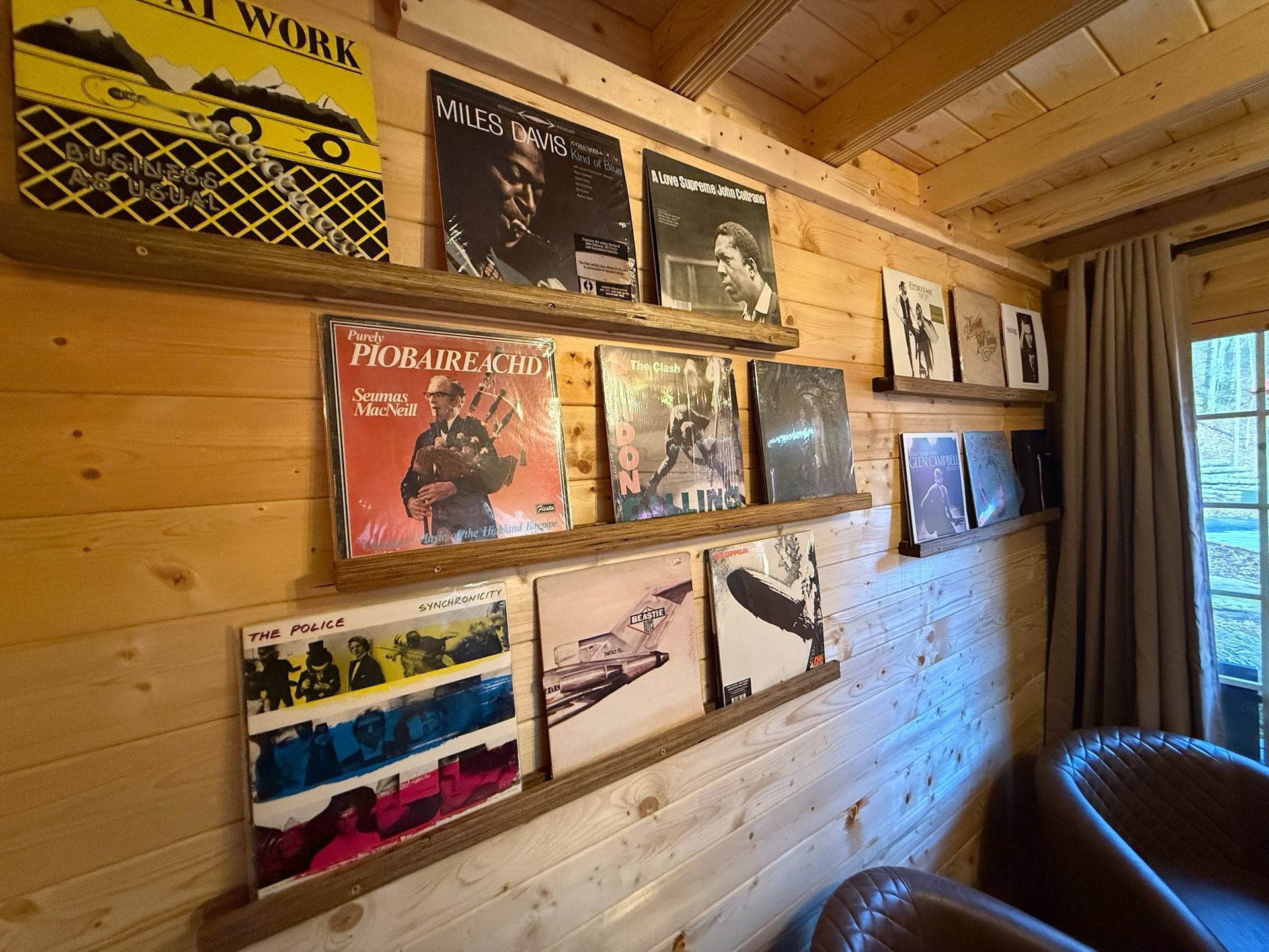 Vinyl album covers displayed in a rustic wooden room with a leather chair and window on the right