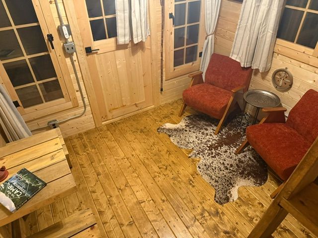 Cozy wooden cabin room with red chairs, small table, rug, and glass doors.