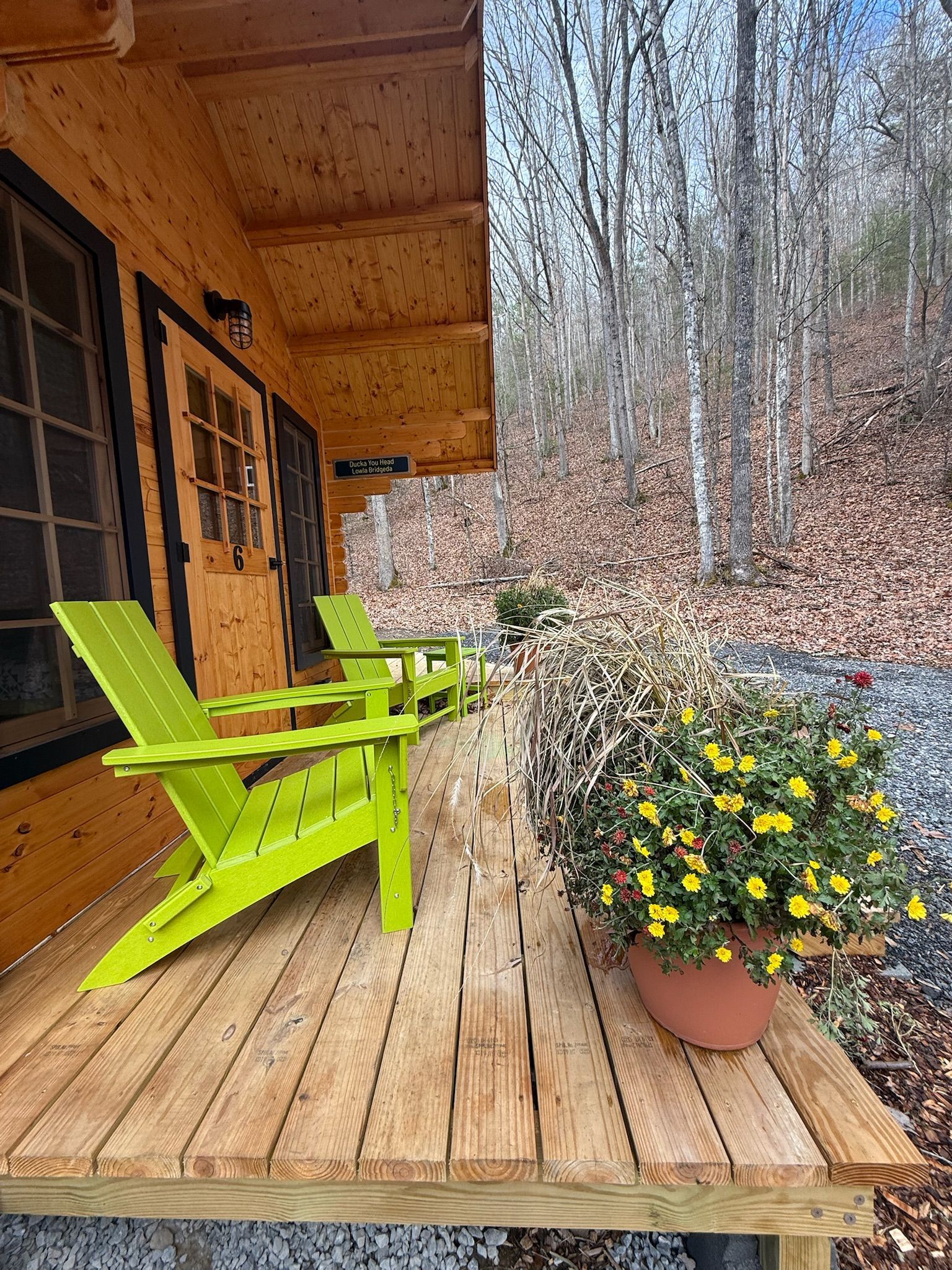 Wooden cabin porch with lime-green chairs and a yellow flower pot overlooking bare trees