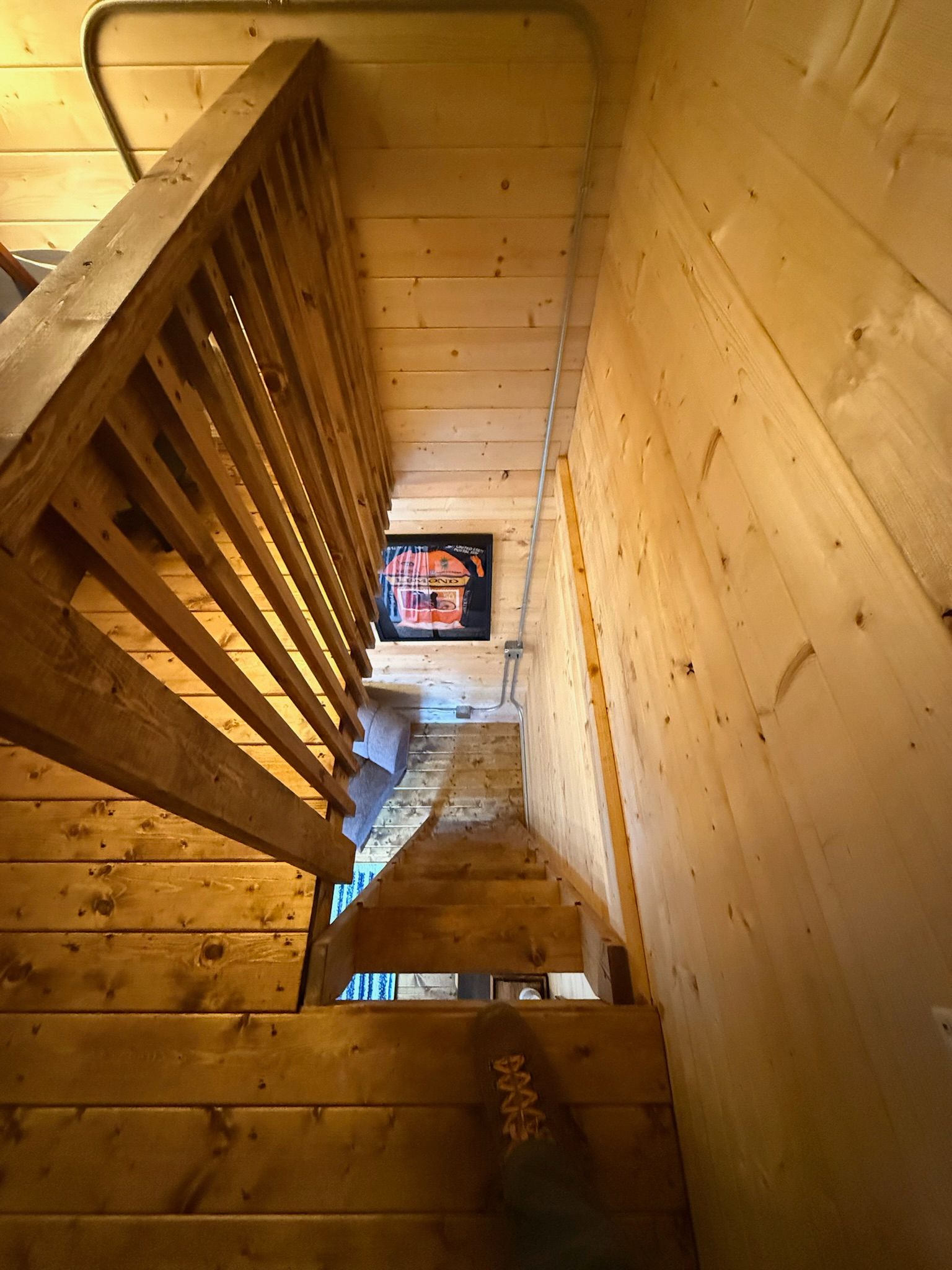 Wooden staircase viewed from above in a rustic cabin, with light wood walls and a small window below.