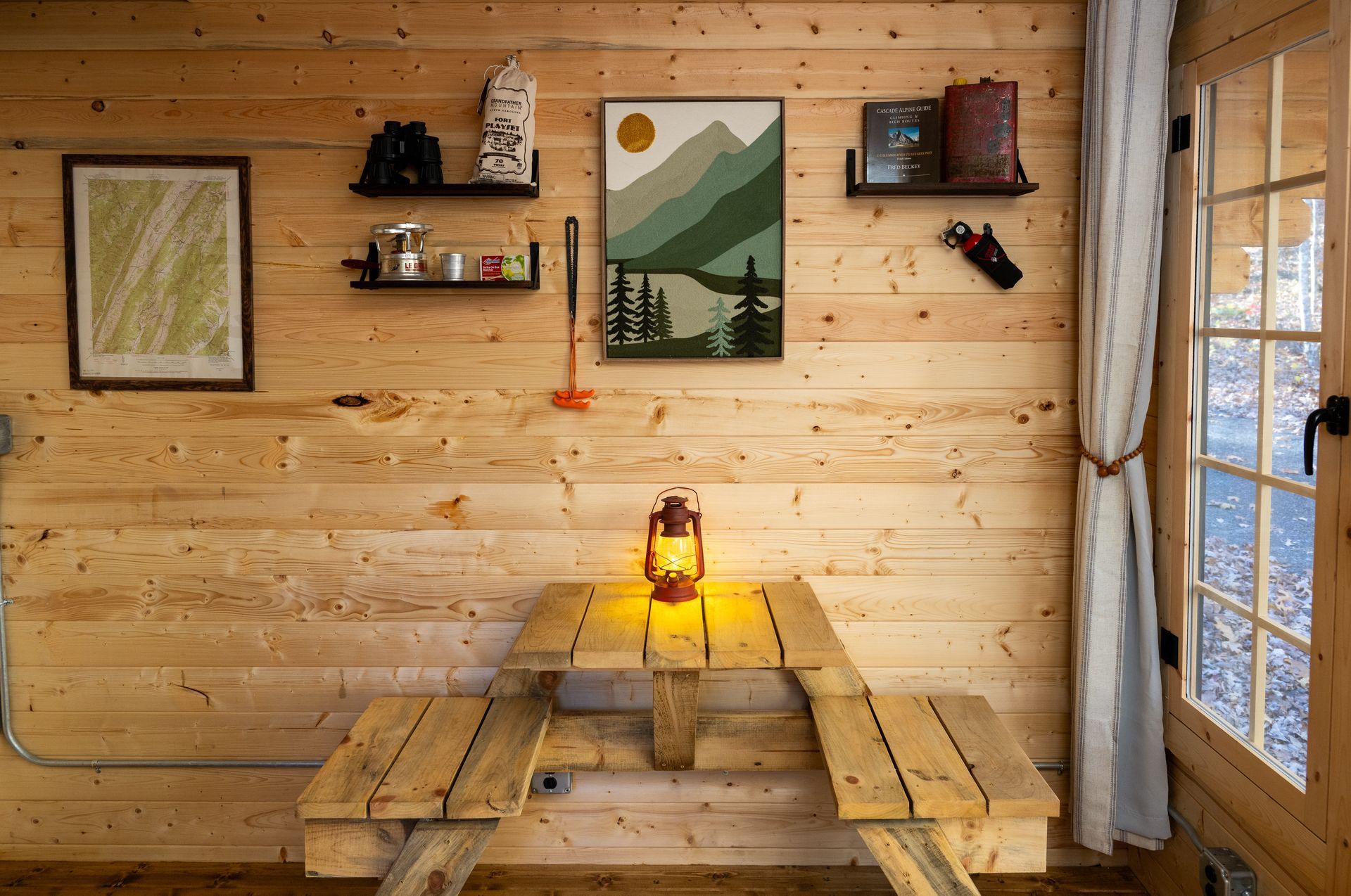 Cozy wooden cabin nook with rustic table, lantern, wall art, and window light