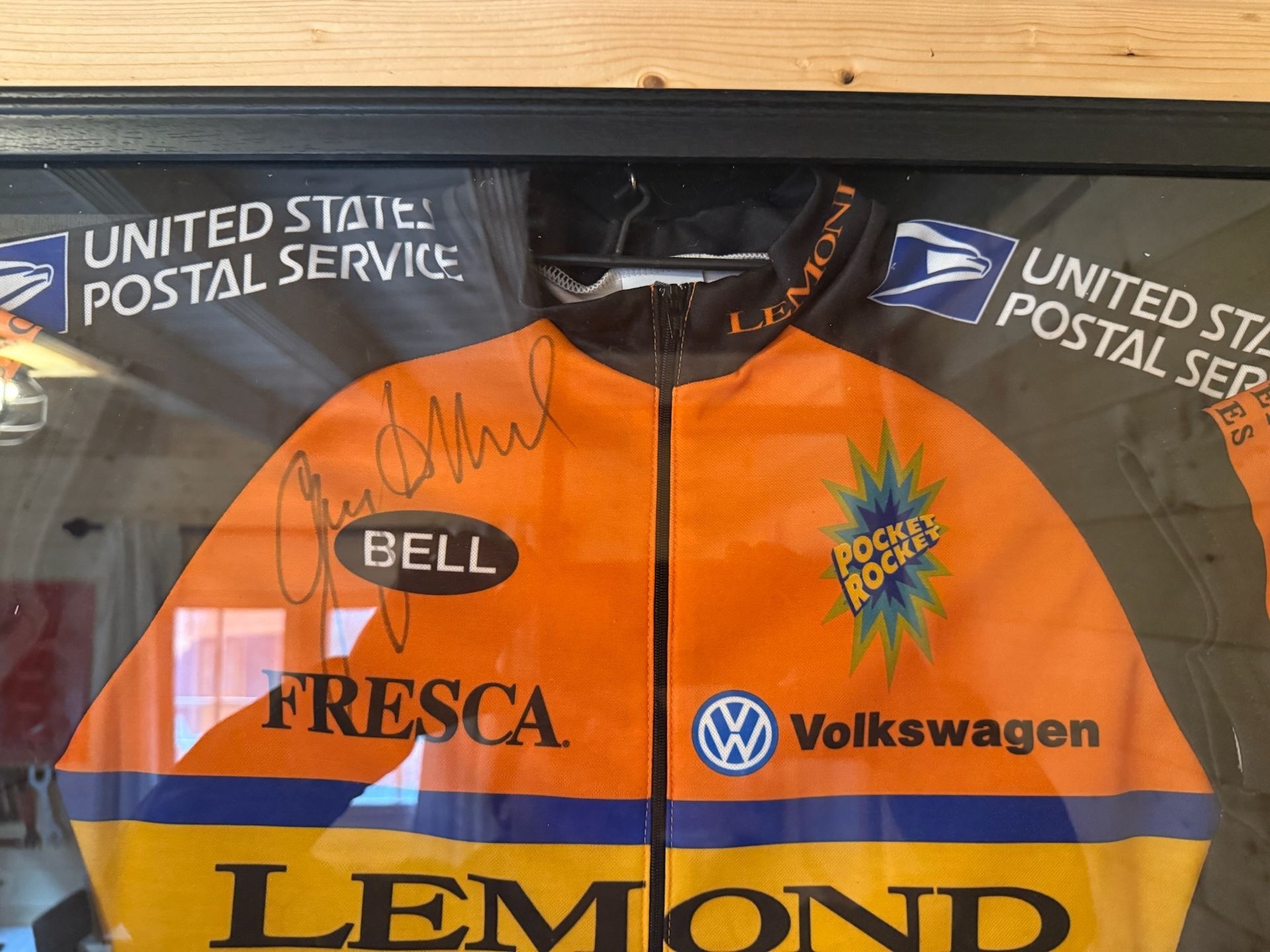 Orange-and-blue Volkswagen Bell Sports Lemond cycling jersey hanging in a display case.