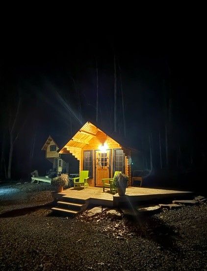 Small warmly lit cabin at night, with steps and porch glow in a dark outdoor setting
