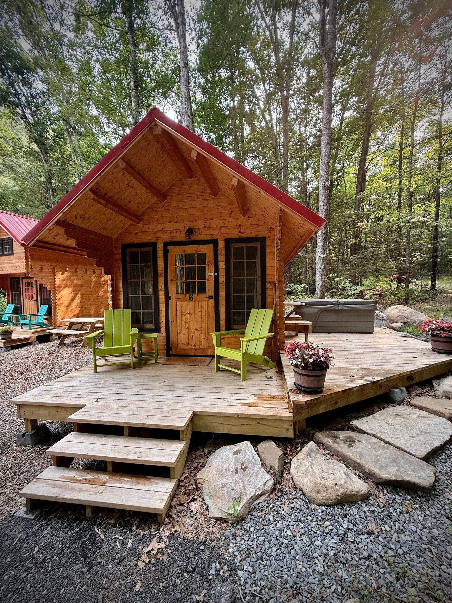 Rustic wooden cabin with red roof, front porch, and green chairs in a wooded setting