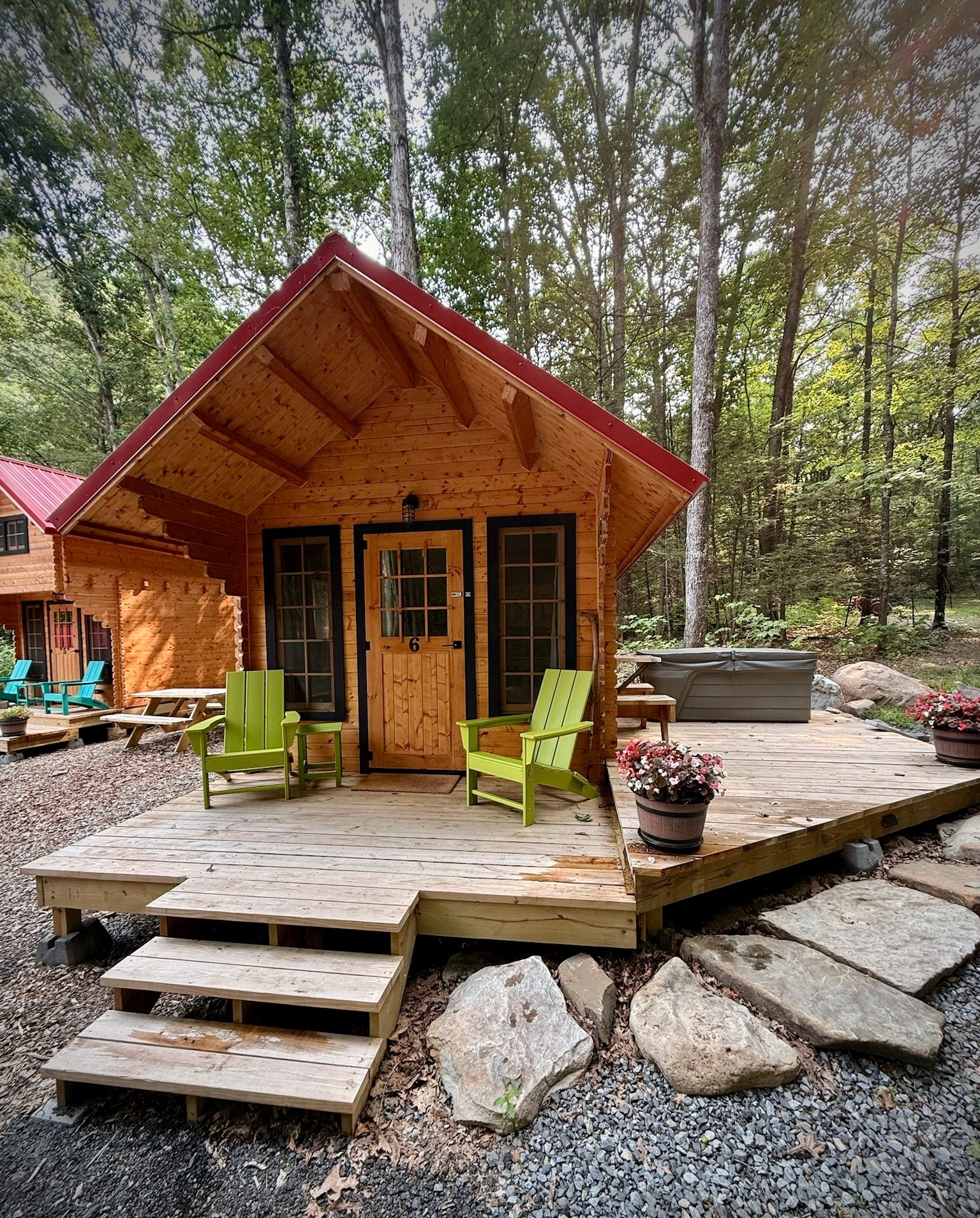 Small wooden cabin with a porch, lime green chairs, and stone steps in a wooded setting
