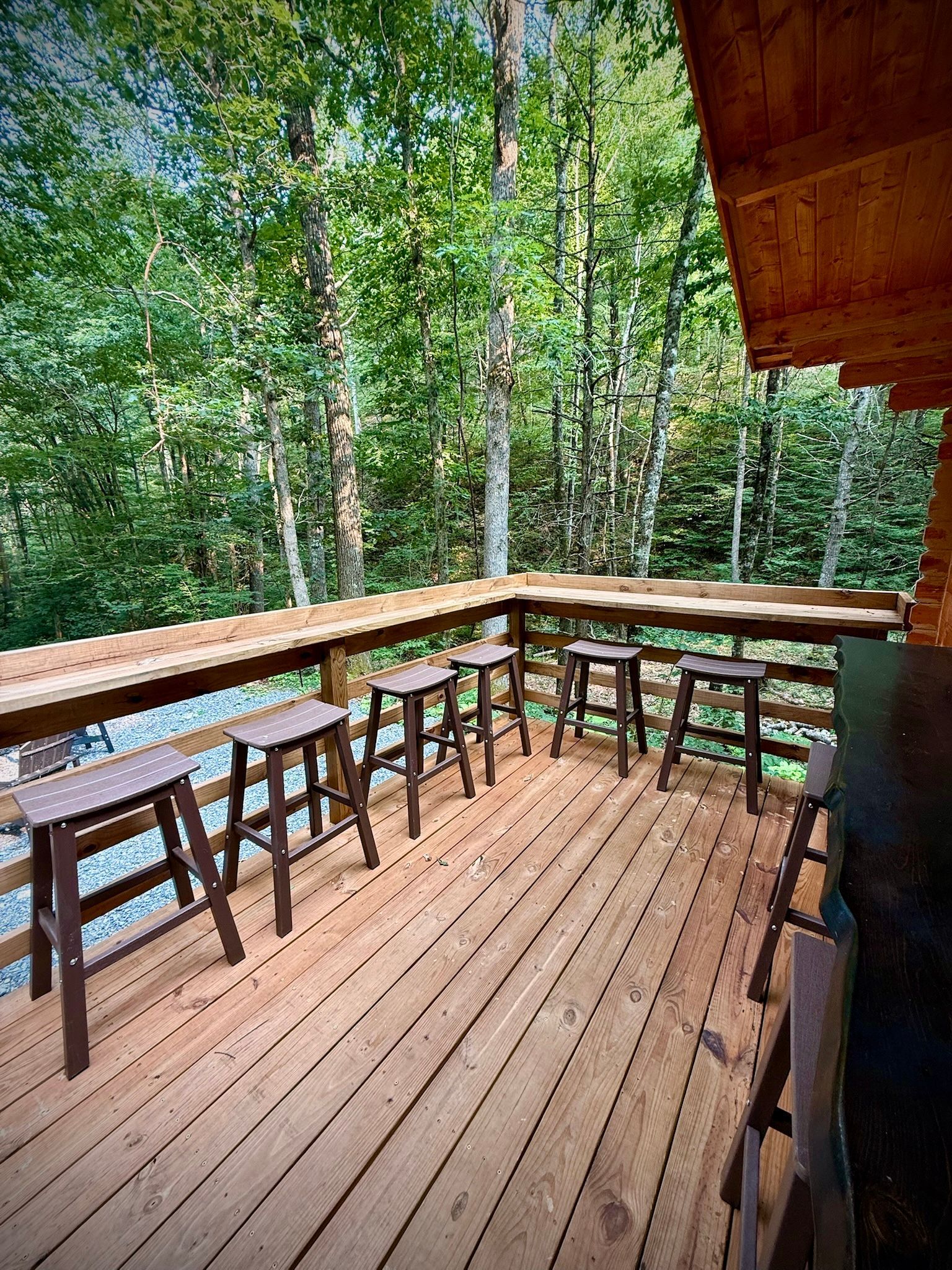 Wooden deck with stools and railings overlooking a lush green forest