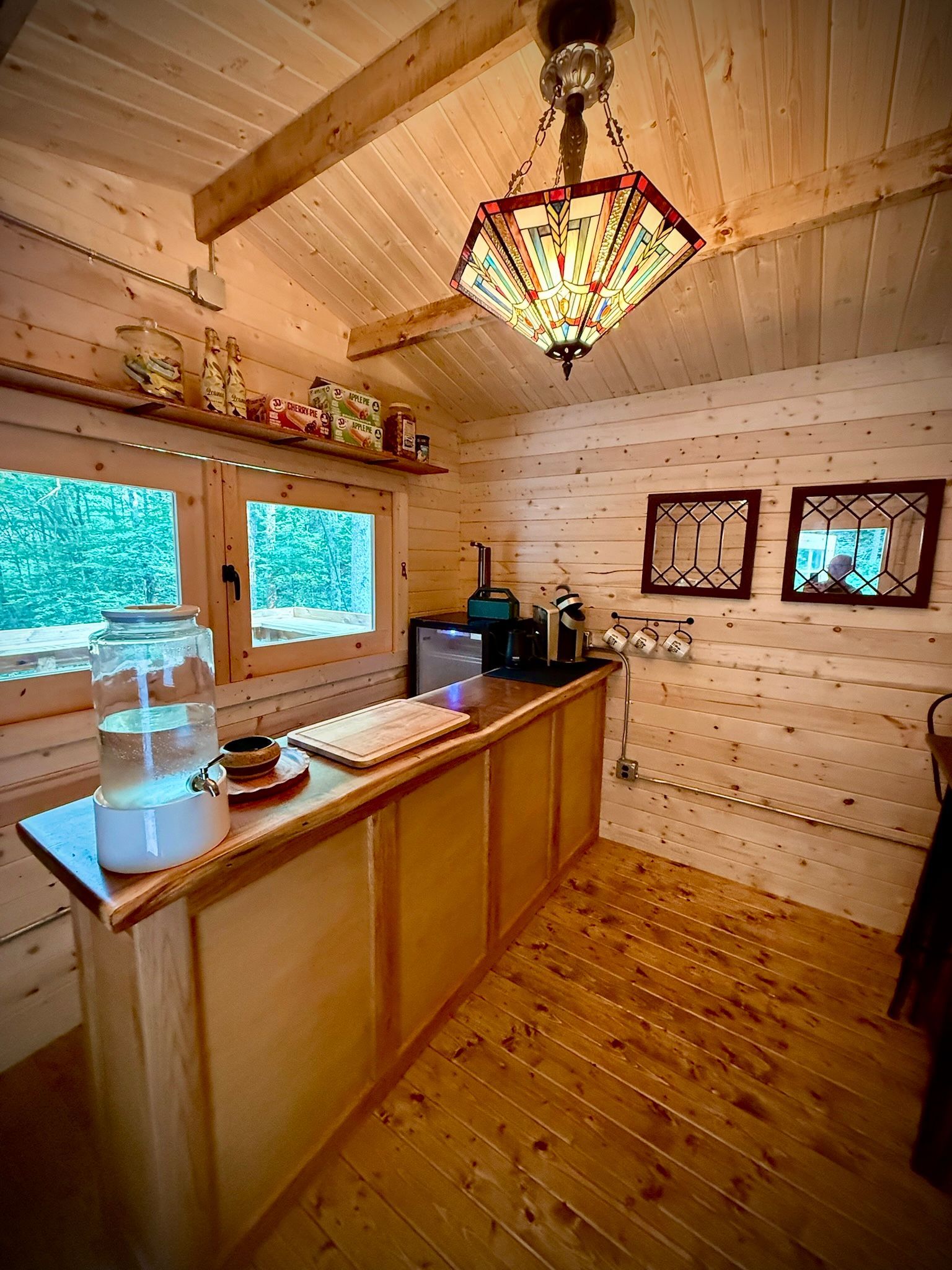 Wooden cabin kitchen with windows, sink, counter, and a hanging stained-glass light fixture.
