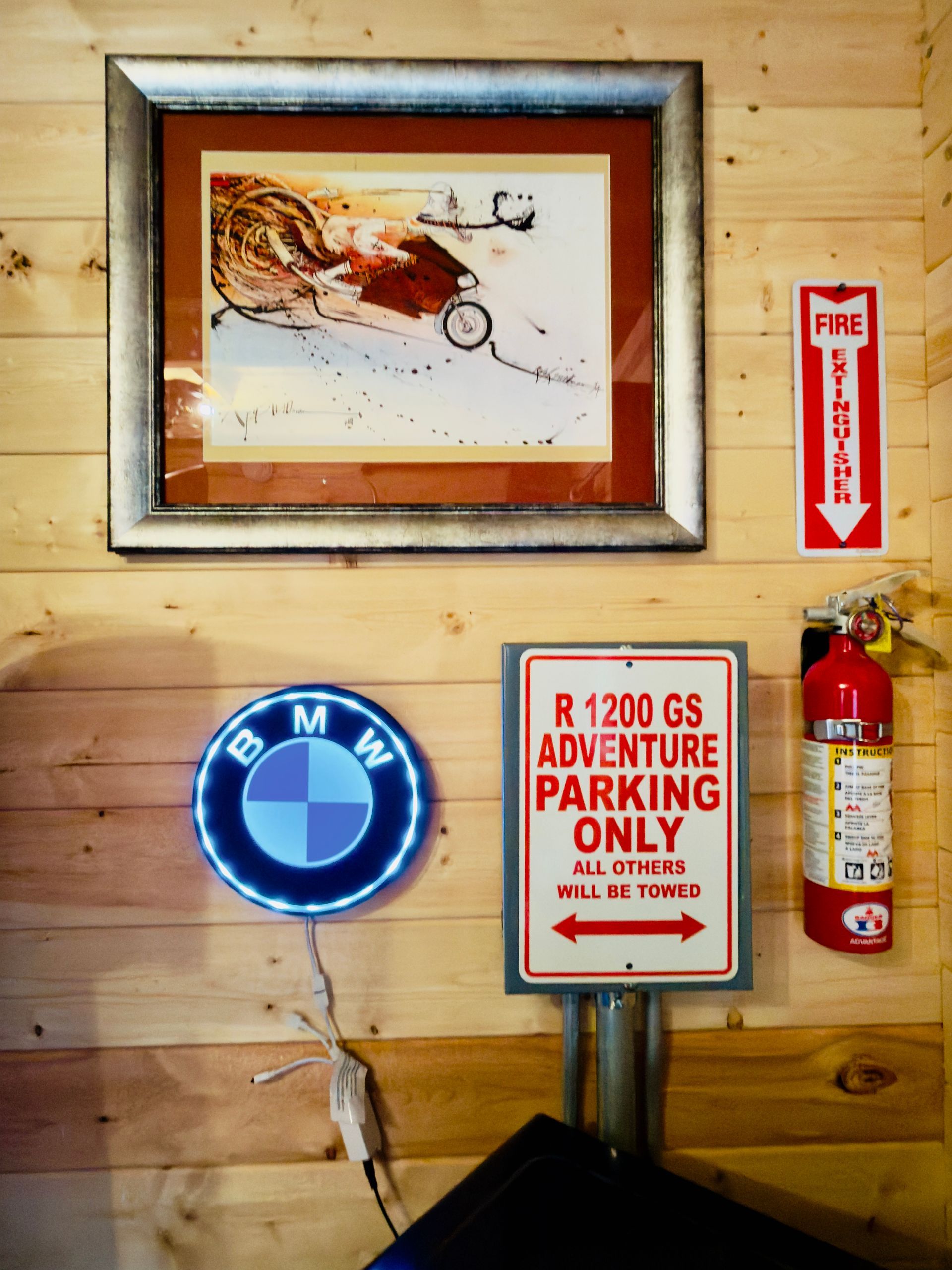 Wood-paneled wall with framed art, BMW logo, RV parking sign, and fire extinguisher.