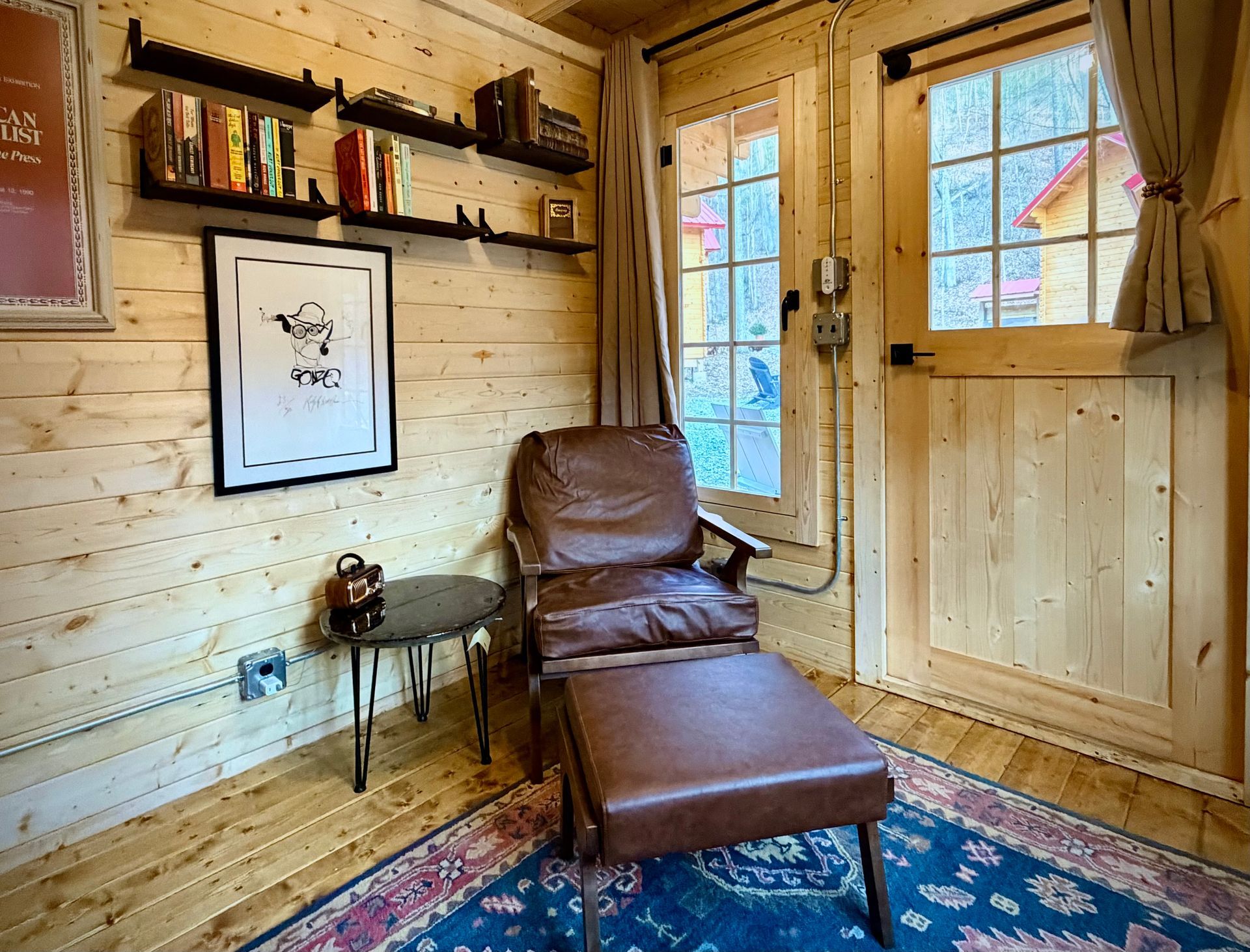 Cozy wood-paneled reading nook with leather chair, chaise lounge, shelves, and sunlit windows.