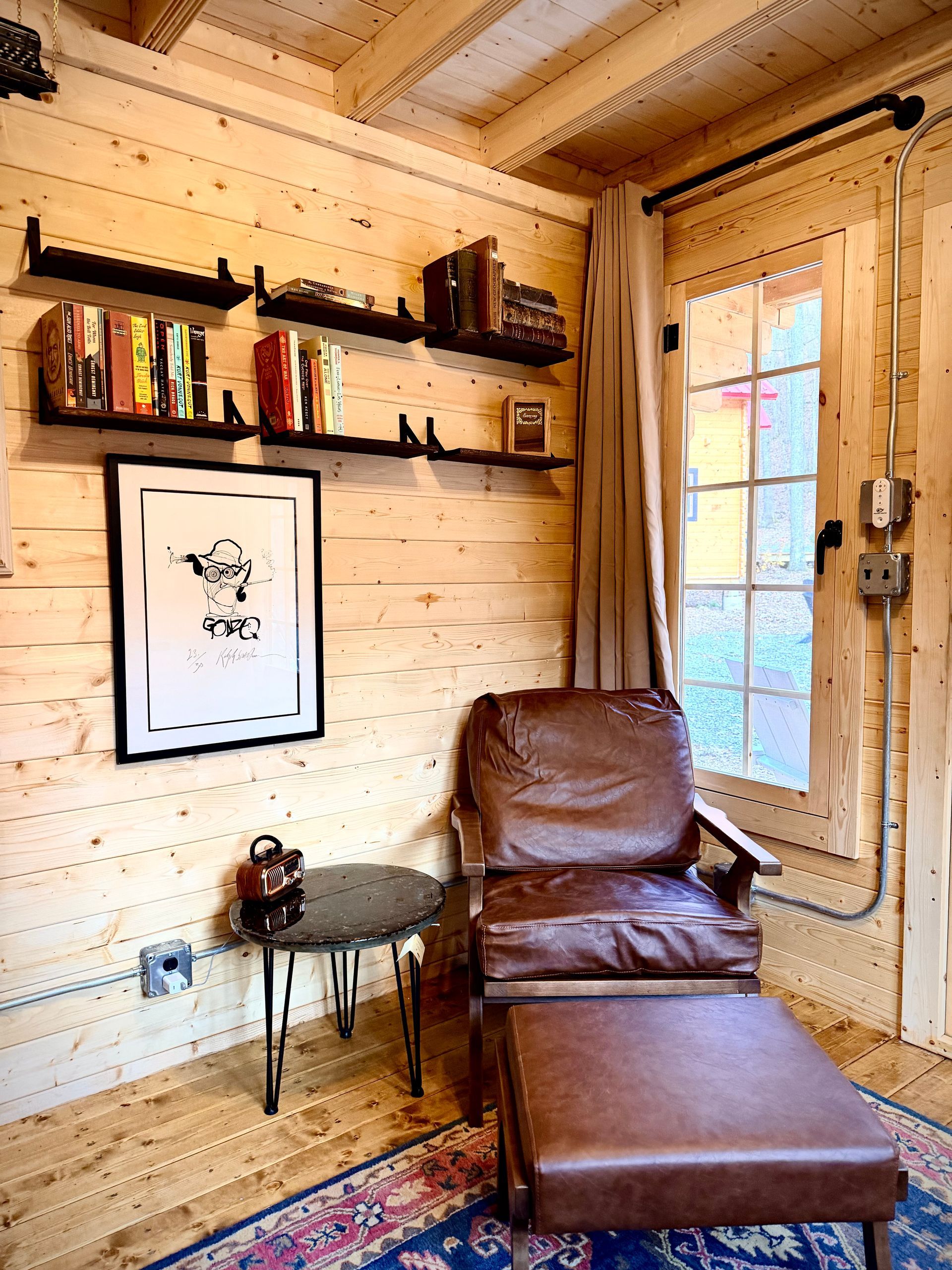 Cozy wood-paneled room with leather chair, ottoman, wall shelves, framed art, and a window.