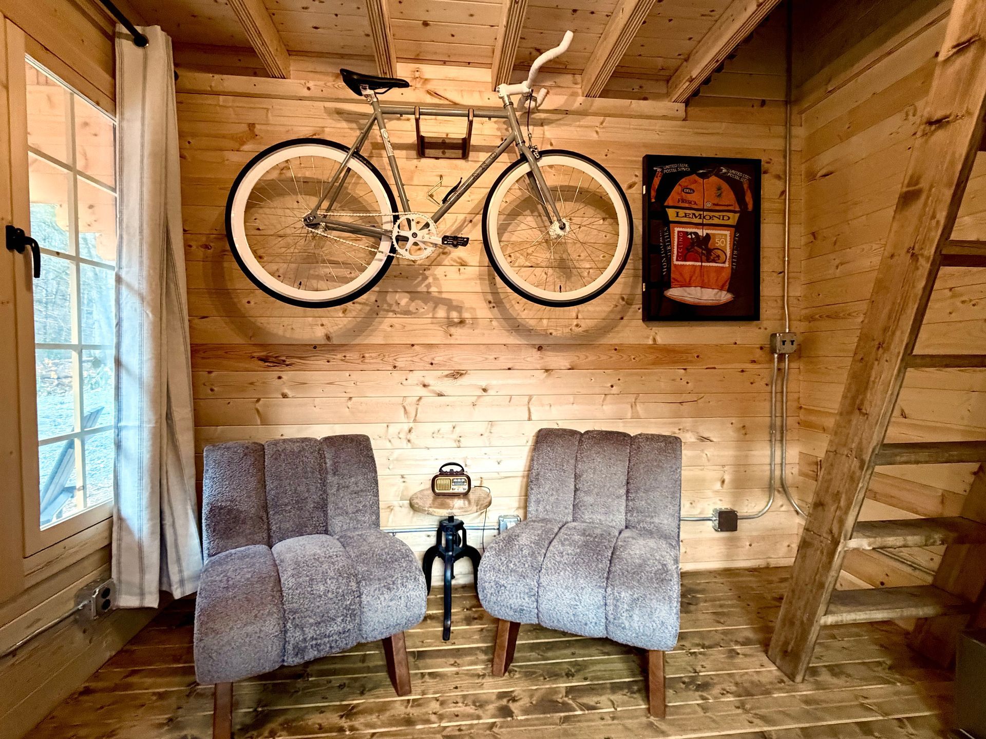 Cozy wooden cabin with two gray chairs, a small table, wall art, and a bicycle mounted above.