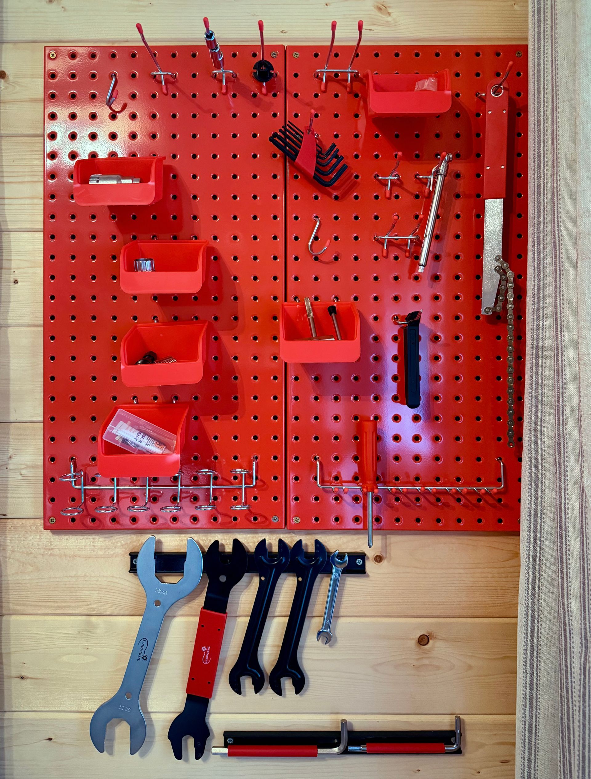 Red pegboard tool organizer with wrenches, pliers, screwdrivers, and hand tools on a wooden wall
